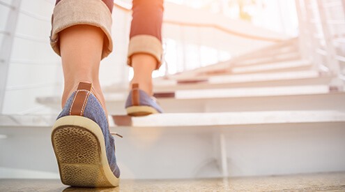 Young adult woman walking up the stairs with sun sport background.